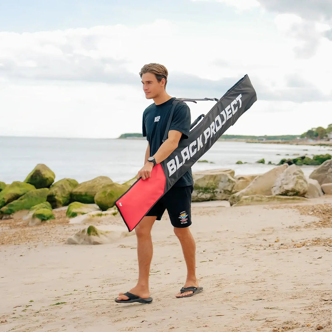 Image of person carrying the Black Project SUP Paddle Bag using the shoulder stap, while walking along the beach.