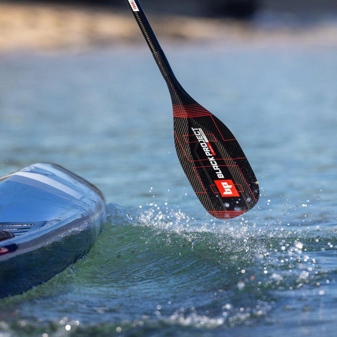 Image shows a Black Project SynergyX Carbon Fiber SUP Paddle in use and about to enter the water.