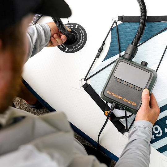 Person using a SUP pump labelled 'Outdoor Master' on a paddleboard with a focus on the device.