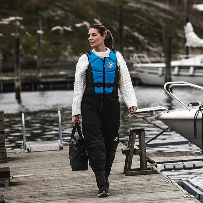 Lifestyle image of a female model wearing a Baltic Hera E.I. Buoyancy Aid in Aqua Blue while walking on a boat pontoon.