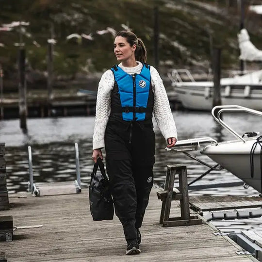 Lifestyle image of a female model wearing a Baltic Hera E.I. Buoyancy Aid in Aqua Blue while walking on a boat pontoon.