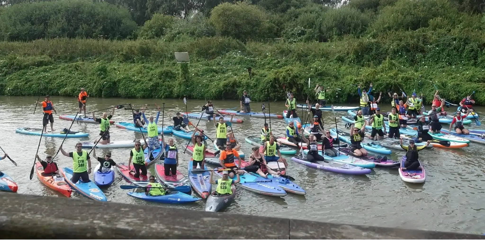 Group of people in kayaks and on paddle boards on a river with greenery in the background