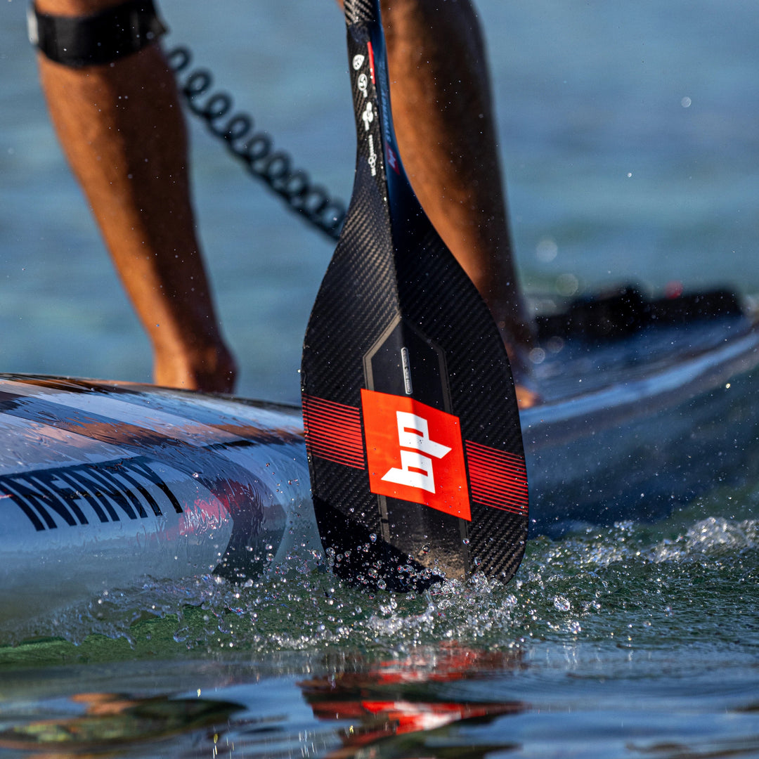 Image shows the front of a Black Project SynergyX SUP Paddle blade. Black carbon fiber SUP Paddle with red logo and design.