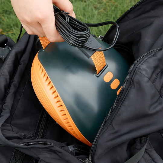 Person holding a black and orange sup pump with a cable, against a black bag background.