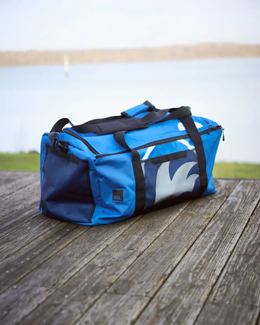 Blue 90L sailing bag with black straps on a wooden surface.