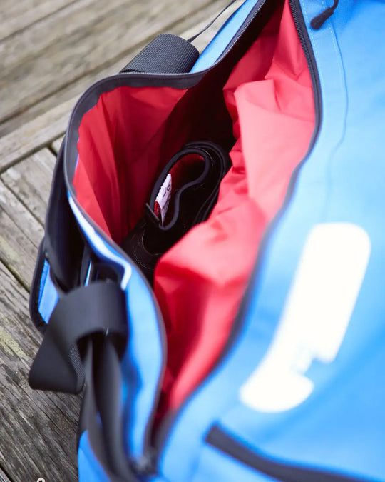 Blue bag with red interior waterproof pocket on a wooden surface.