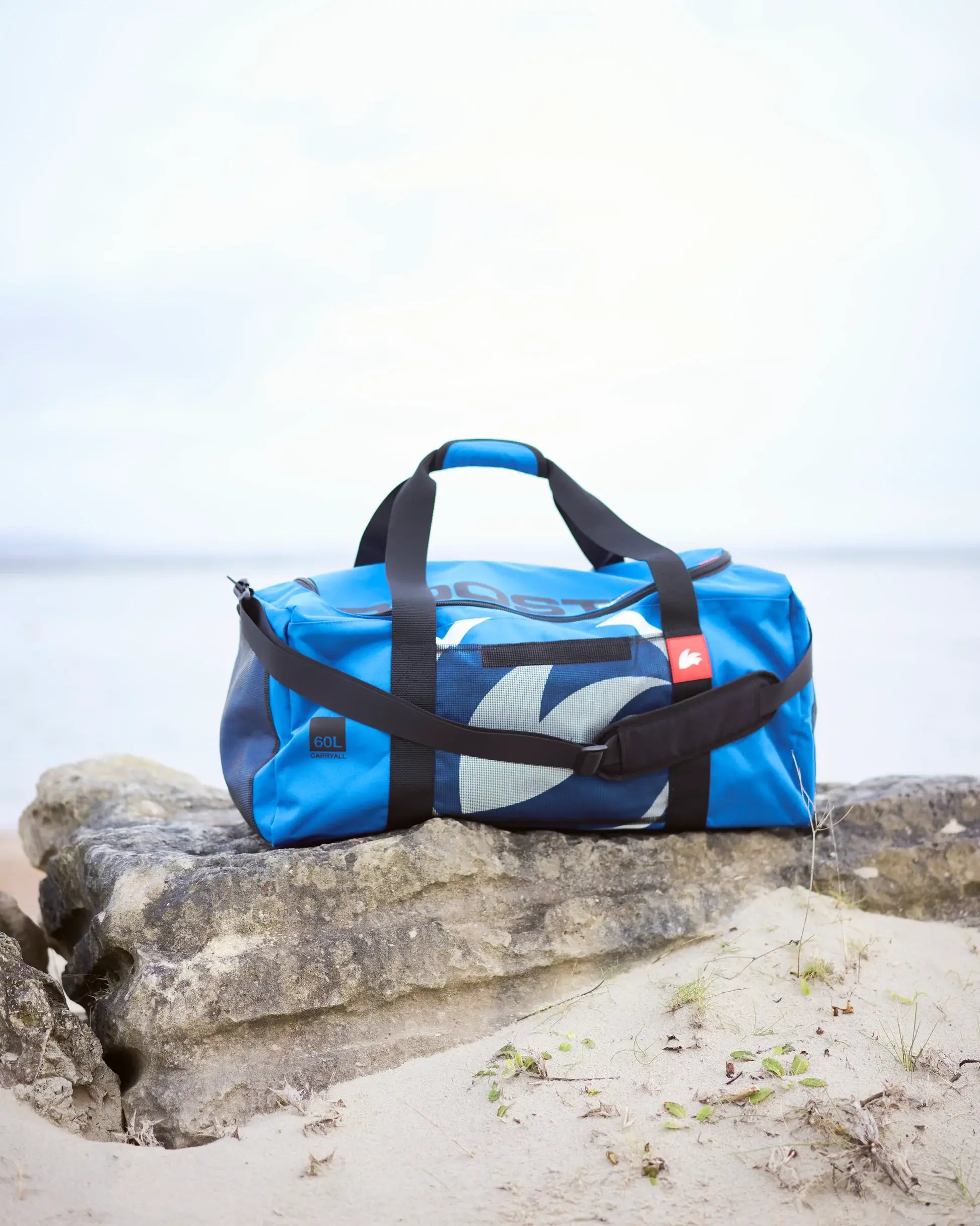 Blue duffel bag with black straps on a rock by the beach.