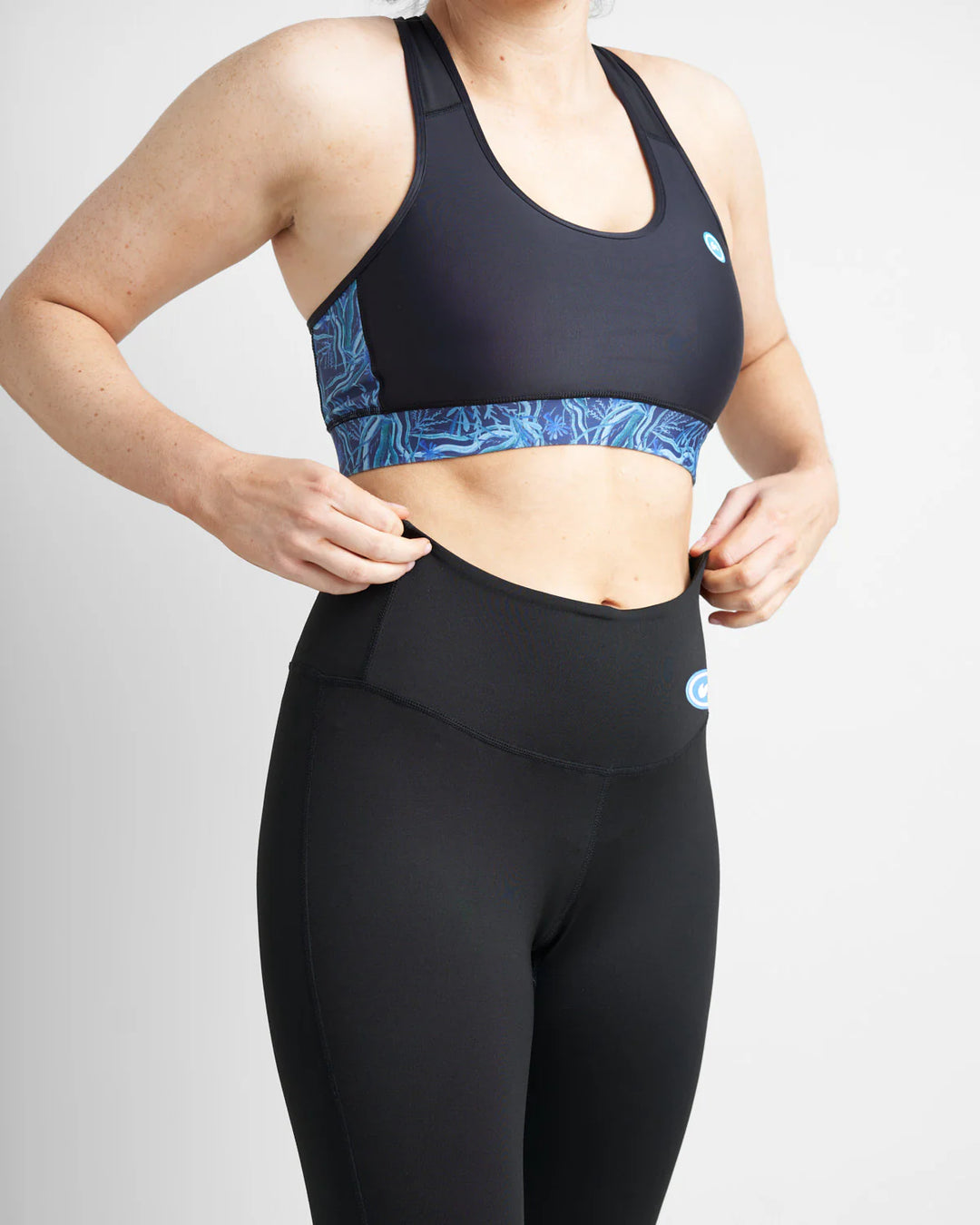 Person wearing a black sports bra and leggings with a blue pattern on a light gray background