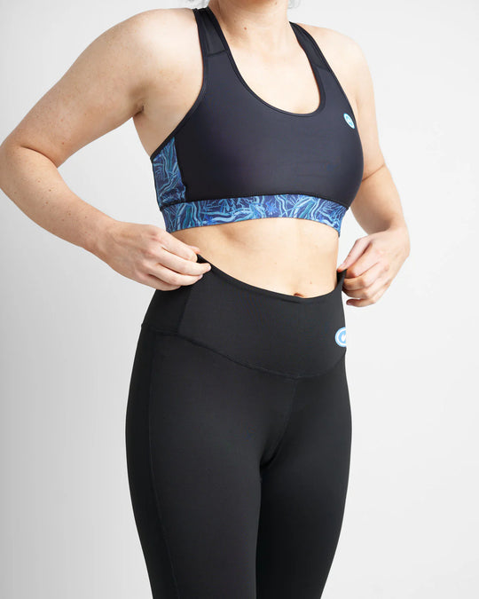 Person wearing a black sports bra and leggings with a blue pattern on a light gray background