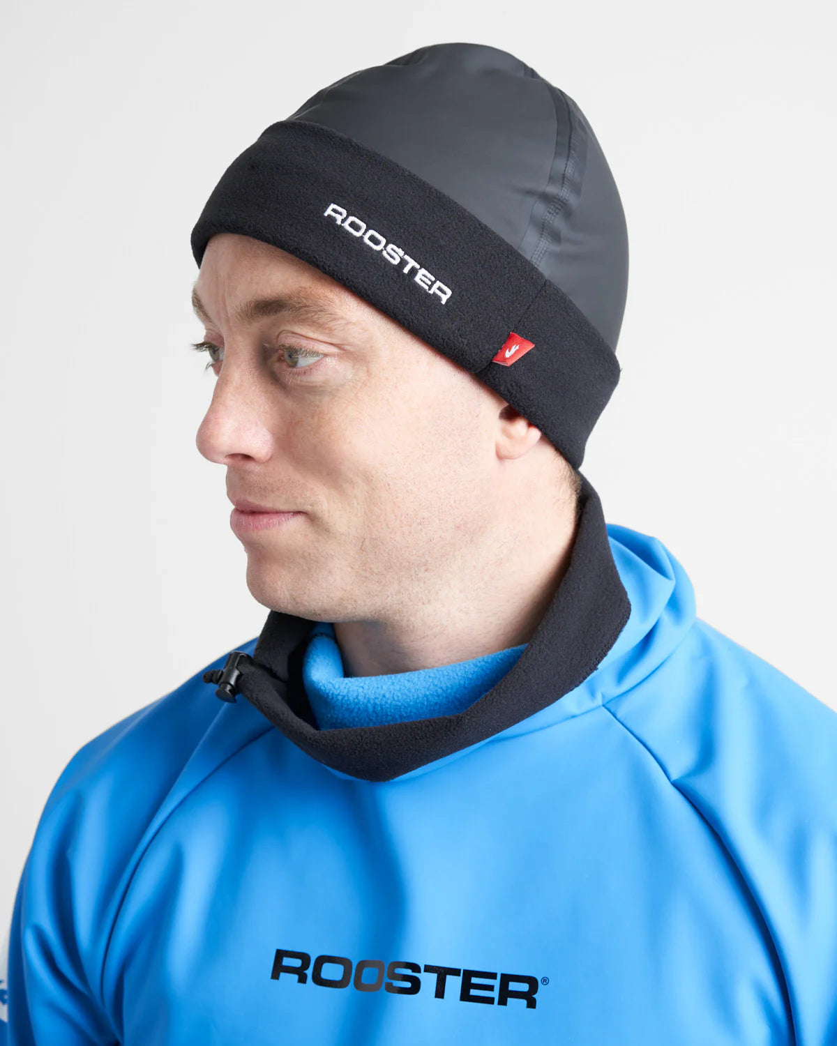 Person wearing a black watersports beanie and blue jacket with 'Rooster' branding on a light grey background.
