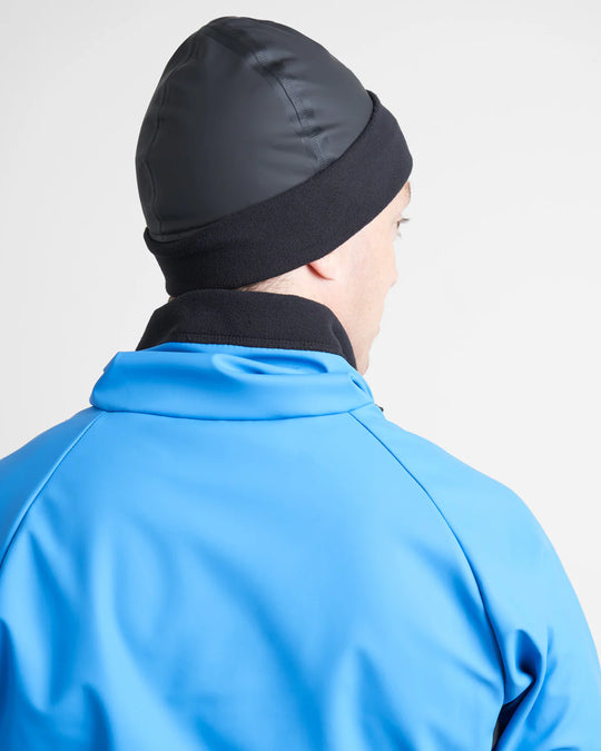 Person wearing a black sailing beanie and blue jacket on a light grey background.