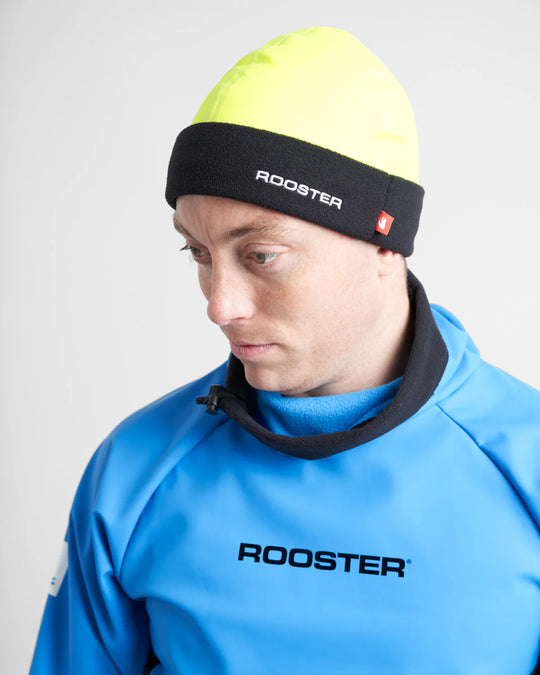 Person wearing a blue Rooster jacket and yellow Aquafllece beanie with black band on a white background.