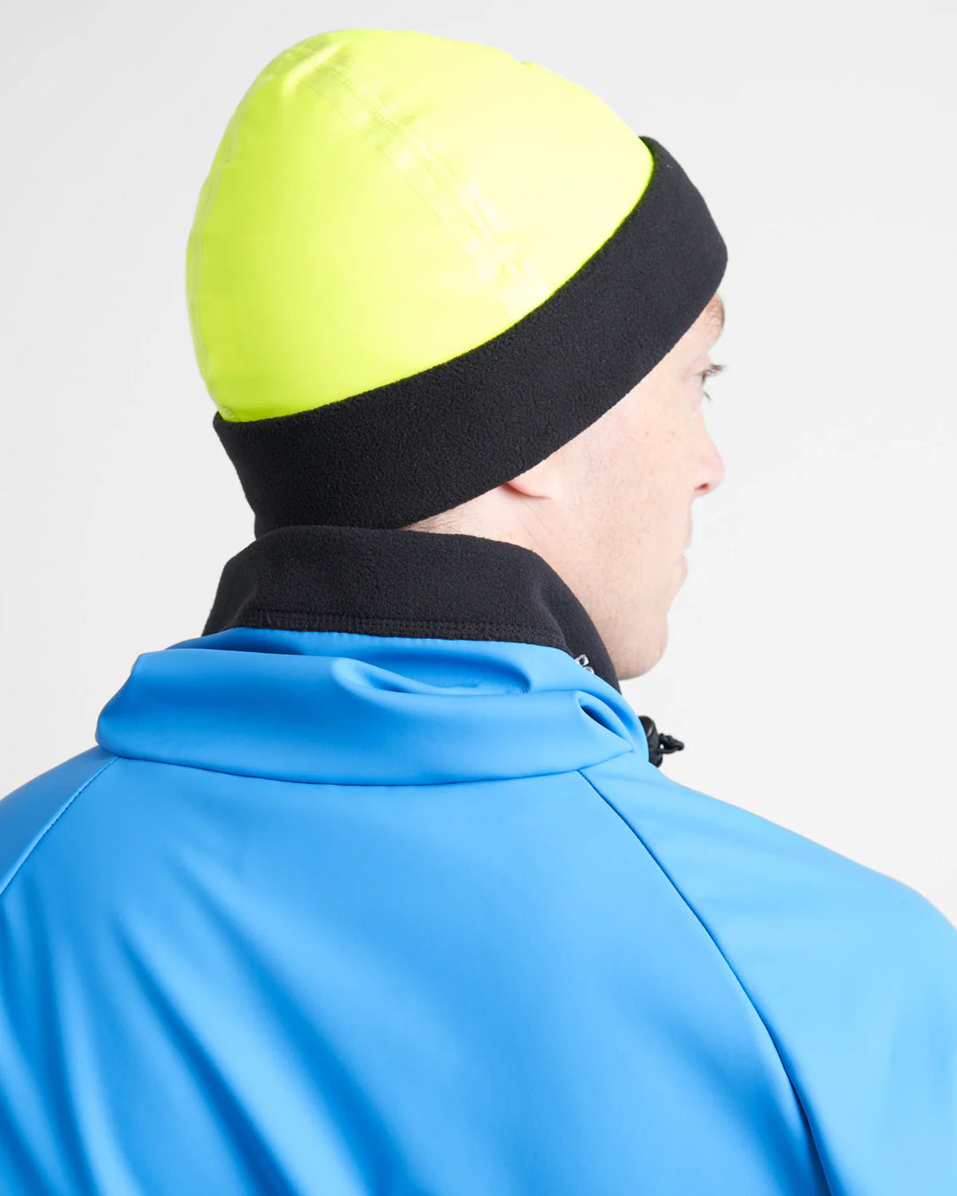 Person wearing a blue jacket and a yellow and black watersports beanie on a light grey background.