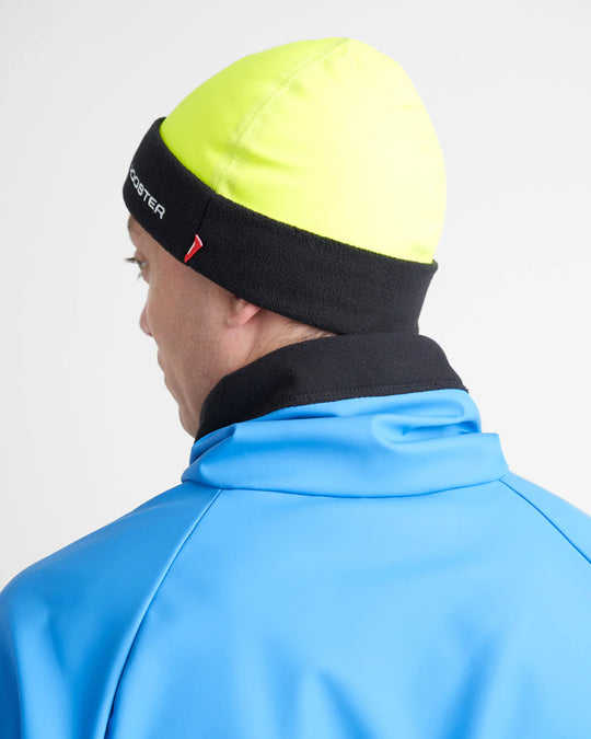 Person wearing a bright yellow sailing beanie with black band and blue jacket on a white background.