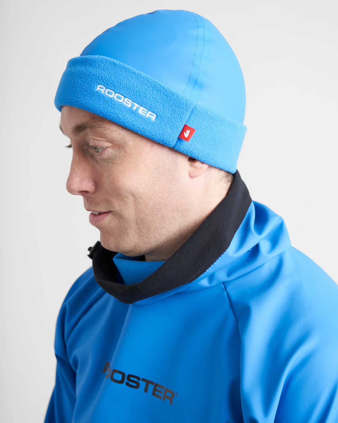 Person wearing a blue Aquafleece watersports beanie and jacket with 'Rooster' branding on a white background.