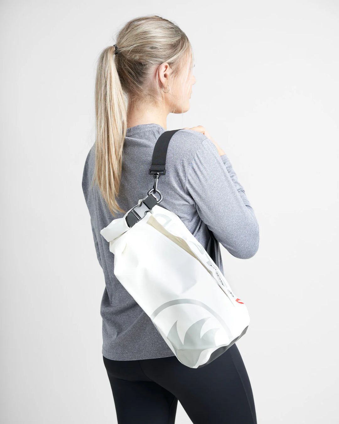 Person wearing a white watersports dry bag with carry strap with a logo on a plain background.