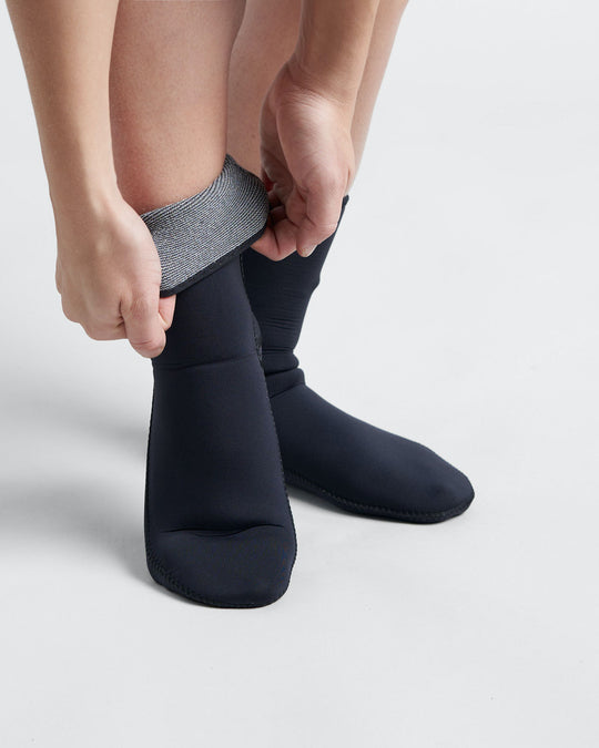 Studio image of the model wearing black 4mm thick neoprene socks with a close up showing the quick dry lining.