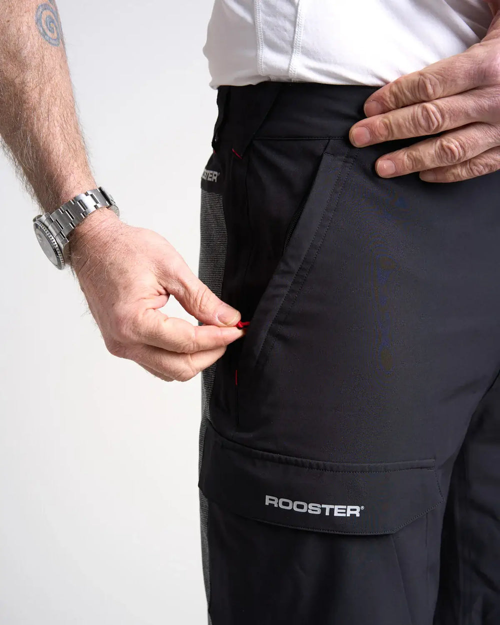 Studio image of a model wearing the black Rooster Technical Shorts 2.0 with a close up of the pocket on a white background.