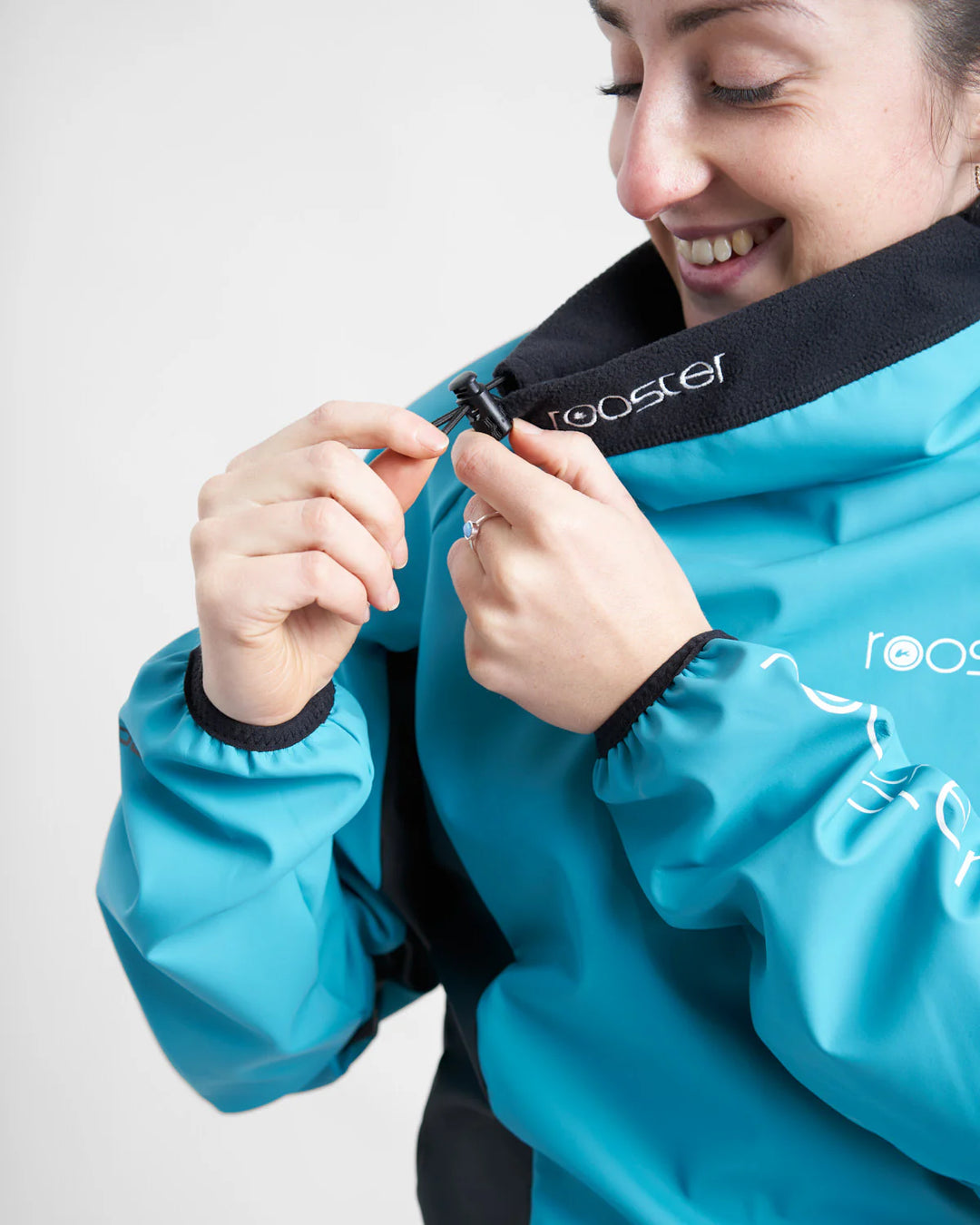 Person wearing a blue water-resistant top with 'rooster' branding, adjusting the neck elastic.