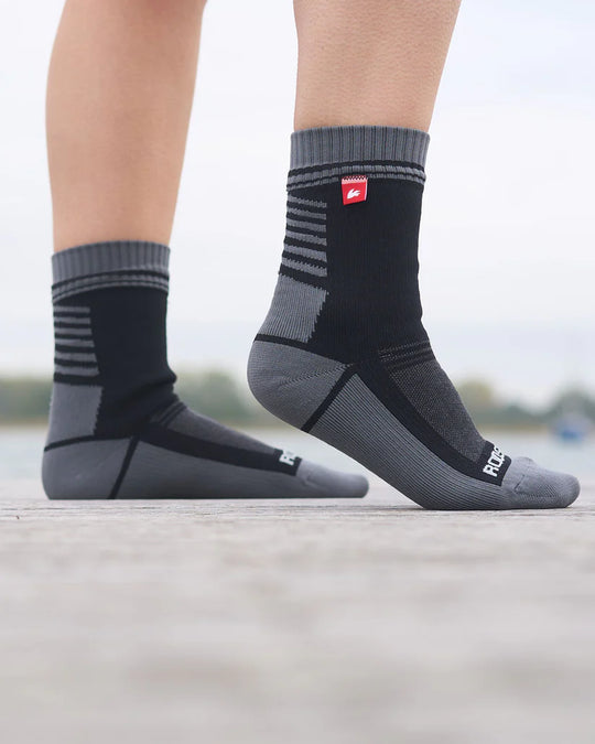 Grey and black waterproof socks with a brand logo worn by a person on a blurred natural background.