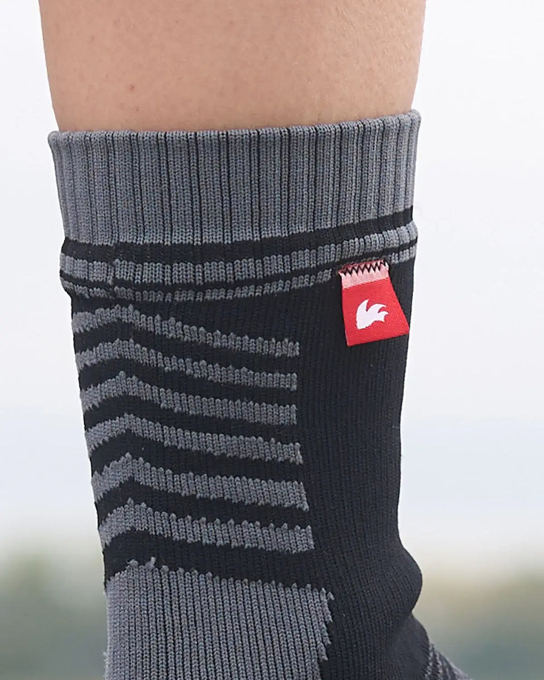 Grey and black striped waterproof sock with a red logo tag on a blurred background.