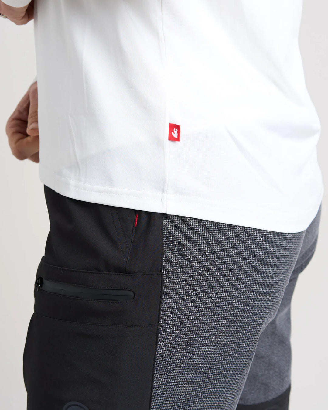White quick dry t-shirt with a red logo worn by a person, paired with black and grey pants on a light background.