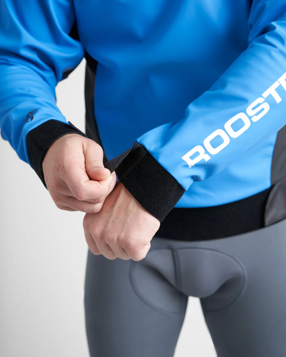 Person wearing a bluedinghy sailing spray top with 'ROOSTER' branding, adjusting a black wristband.