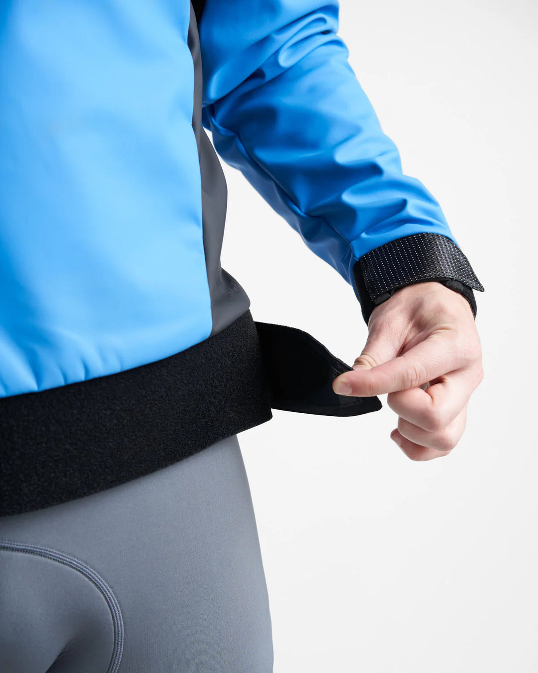 Person wearing a blue Aquafleece Pro Lite Sailing Top with a black waistband, adjusting it against a white background.
