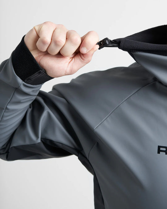 Person adjusting the neck of a grey sailing spray top with a brand logo on a light grey background.