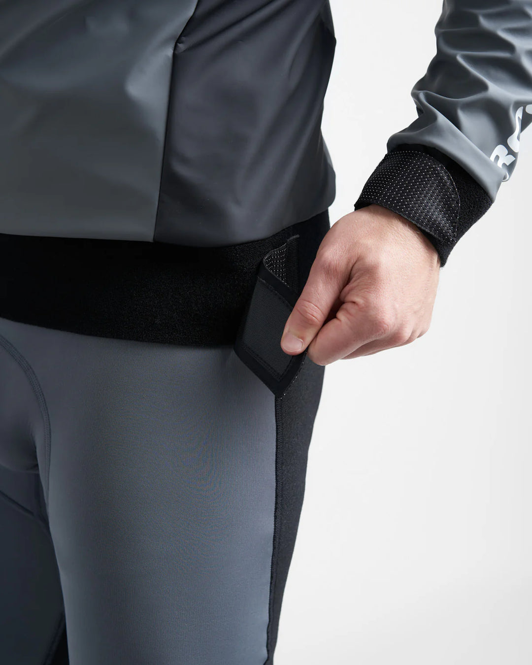 Person wearing a grey Aquafleece top and wetsuit with a black waistband, holding the waistband.