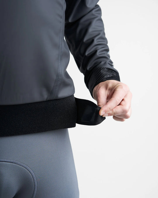 Person wearing a black sailing spray with a black waistband, adjusting it against a white background.