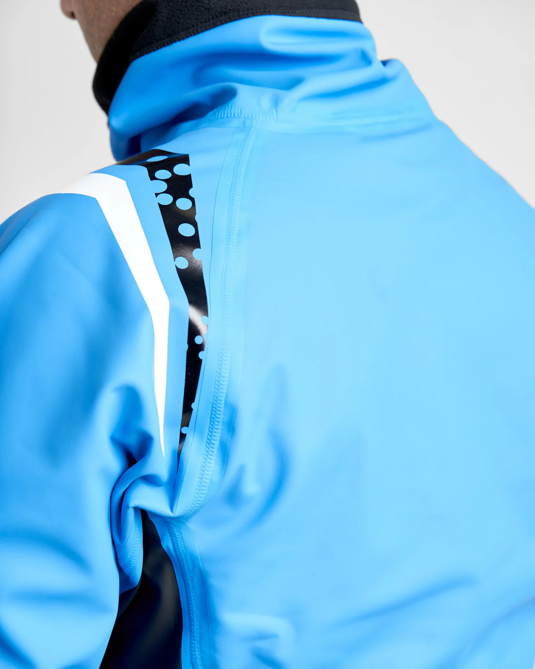 Close-up of a blue watersports spray top with a black and white pattern on the back against a light grey background.
