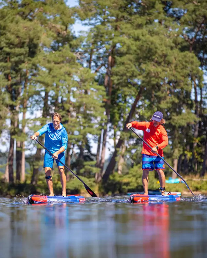 Two people paddleboarding on Starboard All Star Airline Inflatable Paddleboards on a lake with trees in the background