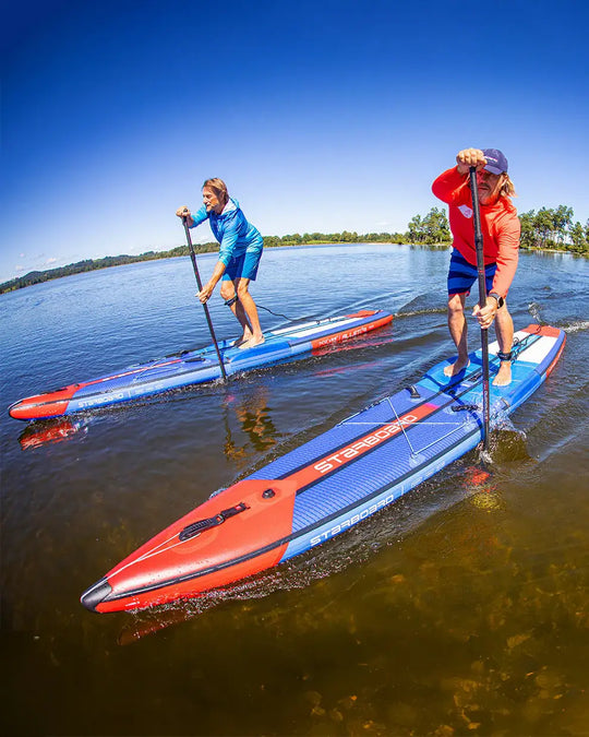 Two people paddleboarding on Starboard All Star Airline's on a lake with clear blue skies.